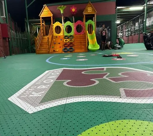 Patio de juegos del Liceo Bicentenario Kronos con piso modular verde, juegos infantiles y el logo del liceo en el piso