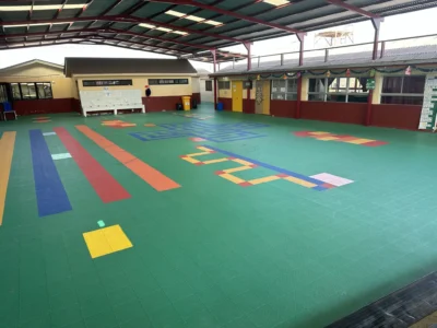 Patio techado de la Escuela Centenario después, con piso modular de colores y juegos