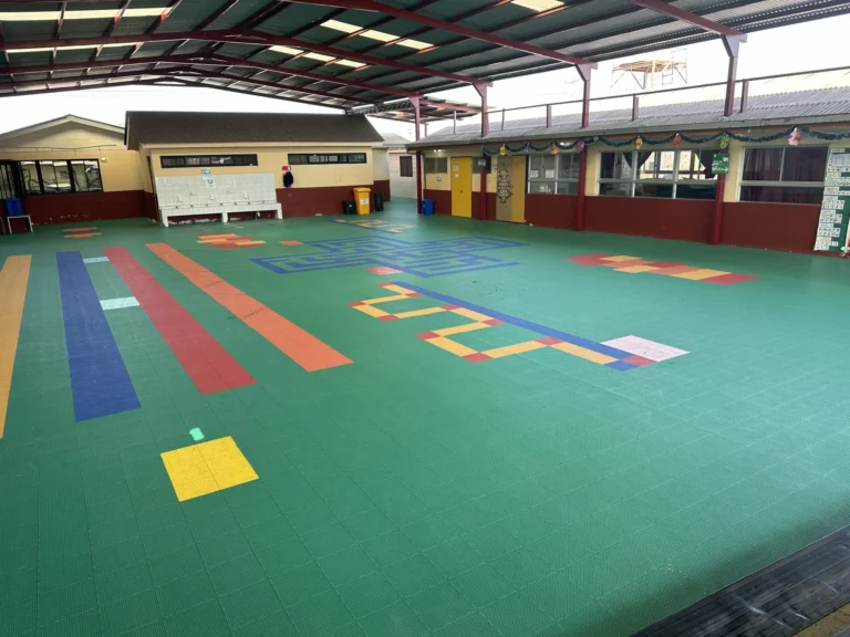 Patio techado de la Escuela Centenario después, con piso modular de colores y juegos